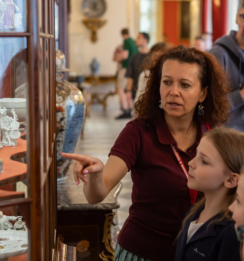 Edukator oprowadzający grupę dzieci po ekspozycji stałej i pokazujący na zawartość witryny w Galerii Porcelany